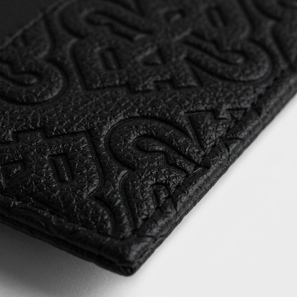 A macro photograph displaying the intricate, debossed signature motif pattern on the black PU material, featuring crisp stitching.