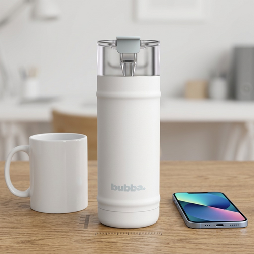 A white Bubba water bottle sits on a desk between a standard mug and a smartphone, demonstrating its size. A graphic ruler is on the desk surface.