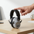 A hand rests on gray fdmt noise reduction earmuffs on a desk, providing a scale reference.